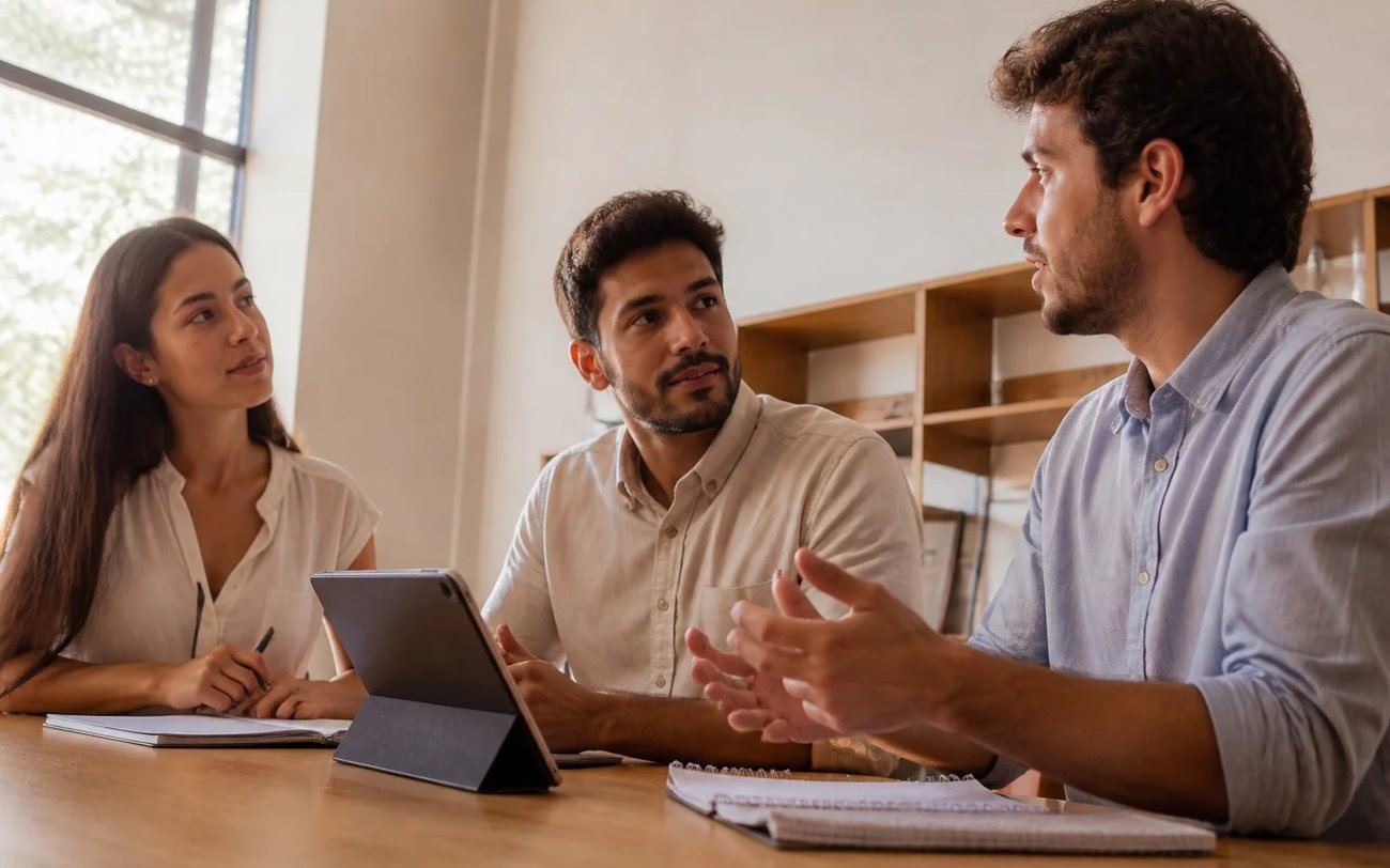 Roda de conversa numa sala clara, com uma pessoa expondo o ponto e duas escutando